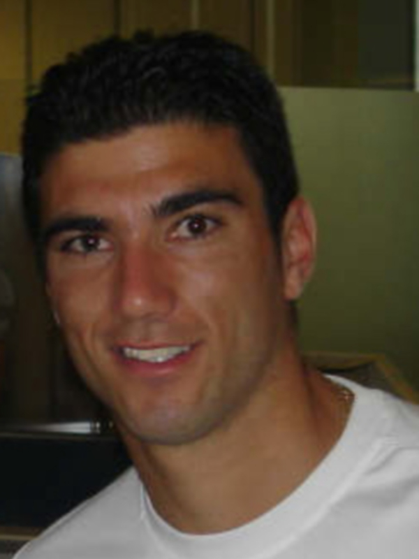 Un hombre con cabello negro y una camiseta blanca sonriendo.