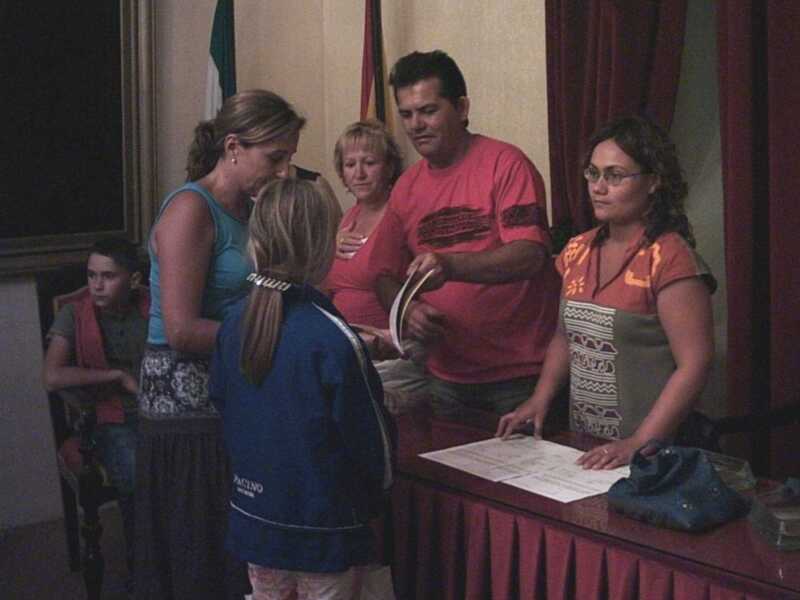 Una familia en una reunión familiar, con un hombre en camiseta roja y una niña en azul, frente a una mesa con documentos.