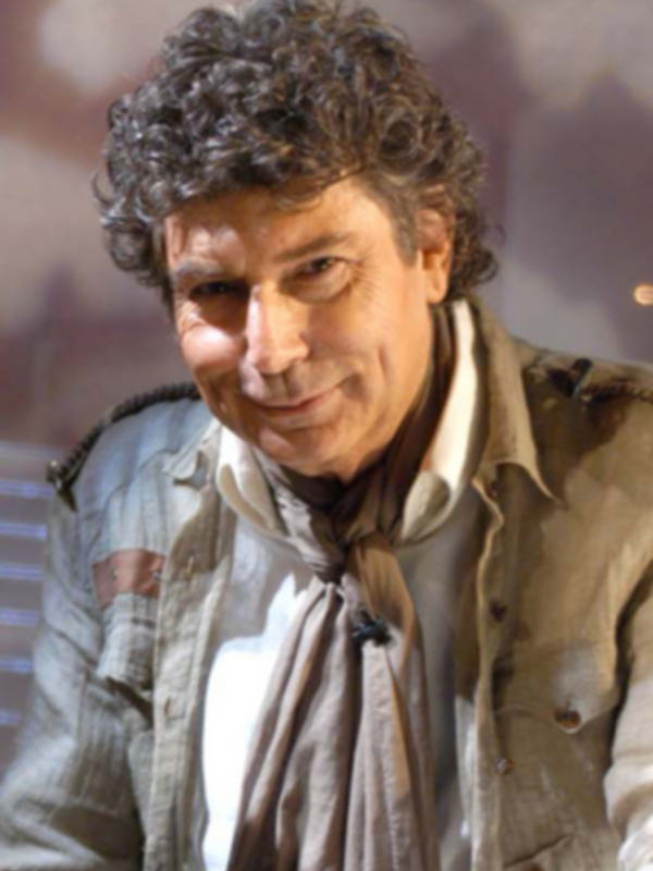 Un hombre con cabello rizado y barba, vistiendo una chaqueta beige con detalles en negro.