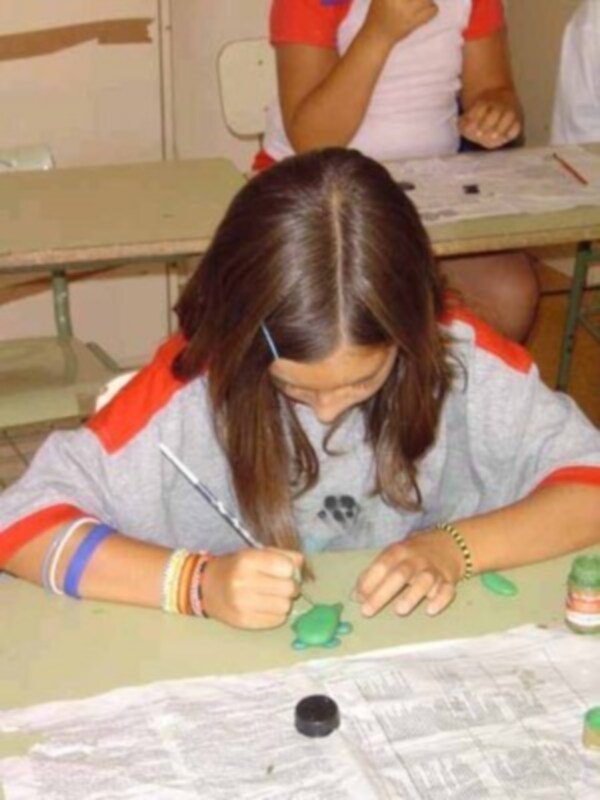 Una niña está dibujando un personaje con plastilina en una mesa cubierta con periódico.