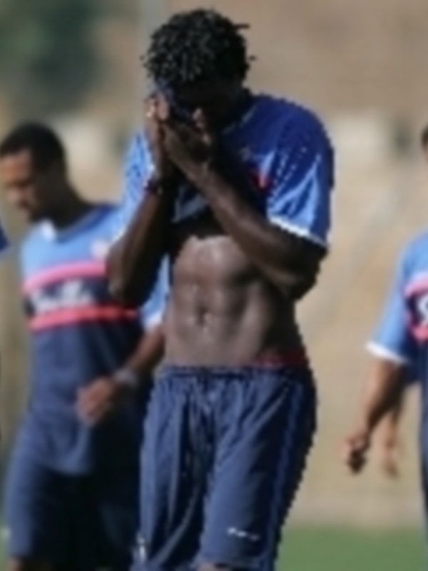 Un jugador de fútbol con una camiseta azul y pantalones cortos, tomando el rostro con la mano.