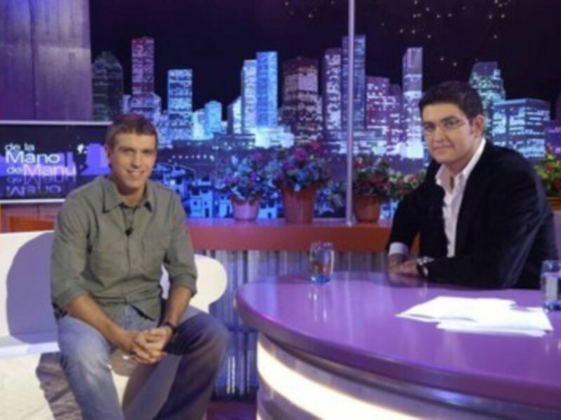 Dos hombres sentados en un set de televisión con una ciudad en el fondo.