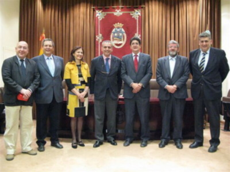 Grupo de personas posando frente a un escudo heráldico en una sala formal.