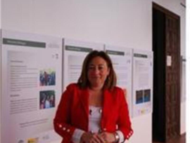 Una mujer en traje rojo está frente a paneles informativos en una exposición.