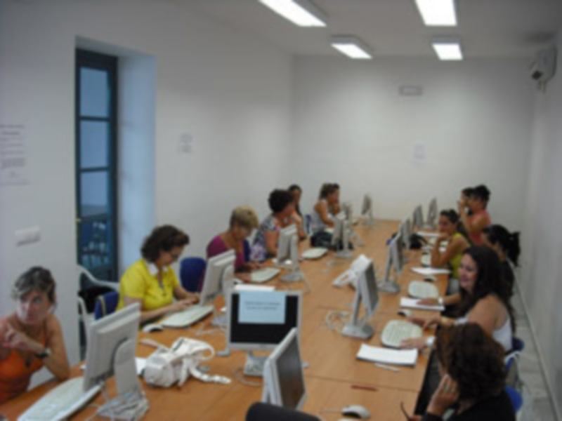 Un grupo de personas sentadas en una sala de conferencias, cada uno frente a un ordenador portátil. La pared está decorada con carteles y una ventana permite la entrada de luz natural.