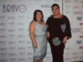 Dos personas posan frente a un fondo con logos de Bravo y Meliá. La persona izquierda lleva un vestido plateado, mientras que la derecha usa una camiseta negra con detalles en blanco.