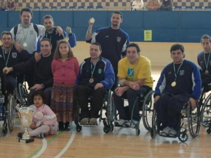 Equipo de baloncesto en silla de ruedas celebrando con trofeo y medallas.