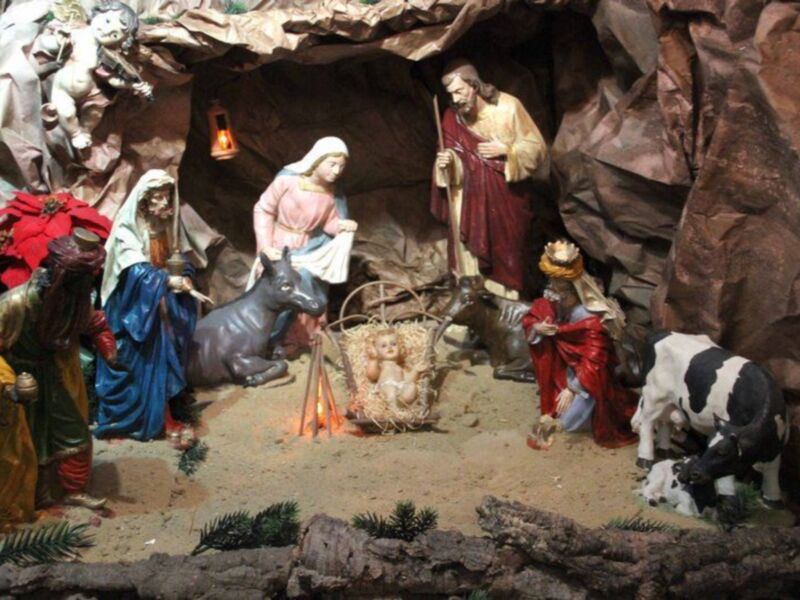 Escena navideña con figuras de la Virgen María, José y Jesús en el nacimiento, rodeados por animales como un burro y una vaca. La escena se desarrolla en un entorno rocoso con luces y detalles que iluminan la escena.