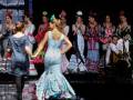 Una mujer en un vestido de flamenca camina por el escenario mientras otros bailarines y músicos se preparan para el siguiente número.