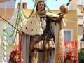 Estatua de San Juan Bautista en procesión, adornada con flores y mantos, durante una celebración religiosa.