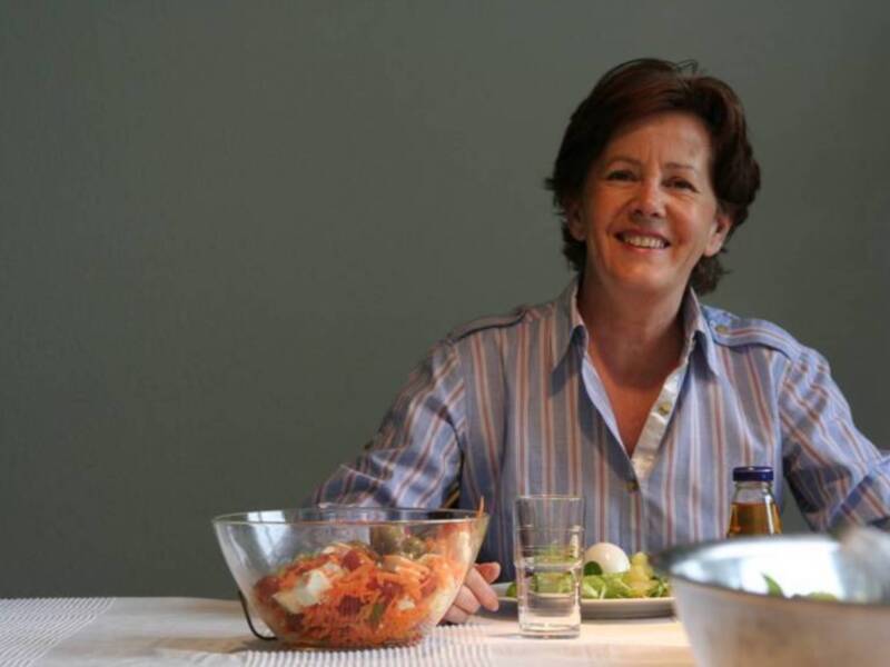 Una mujer sonriente frente a una ensalada en una mesa de cocina.