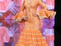 Modela en desfile de moda flamenca con vestido anaranjado con volantes y detalles bordados