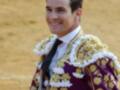 Un matador sonríe en el ruedo, vistiendo un traje de luces tradicional con detalles florales y una corona de flores en el hombro.