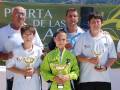 Los niños son ganadores de un torneo deportivo, posando orgullosos con sus trofeos. Detrás de ellos, hay un cartel verde que dice "Puerta de las Aves".