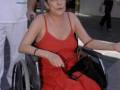 Una mujer en silla de ruedas, vestida con un vestido rojo, camina por una calle.