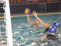 Partida de waterpolo en piscina, jugadores con cascos azules y una pelota multicolor.