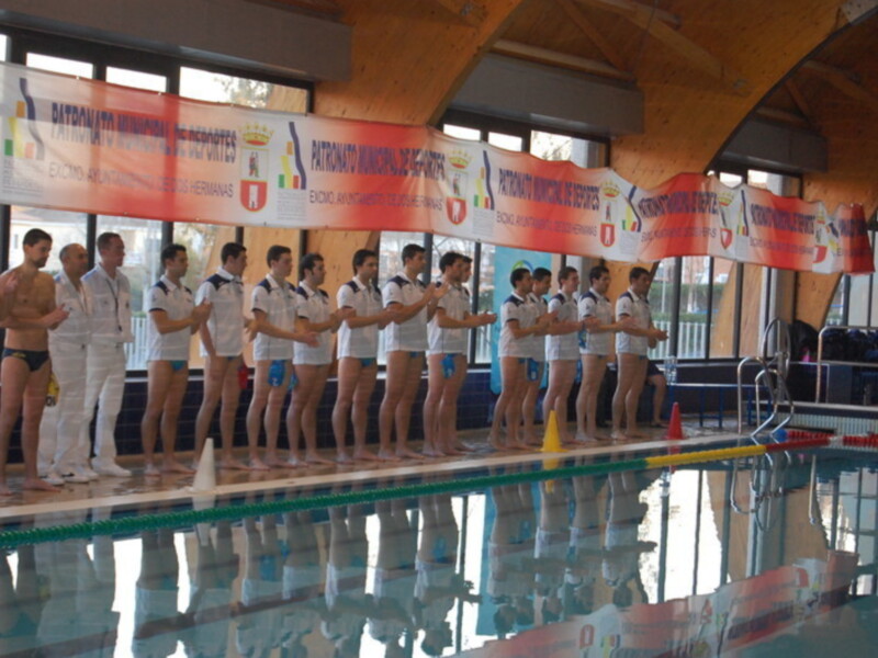 Equipo de natación en una piscina, con un banner de patrocinio al fondo.