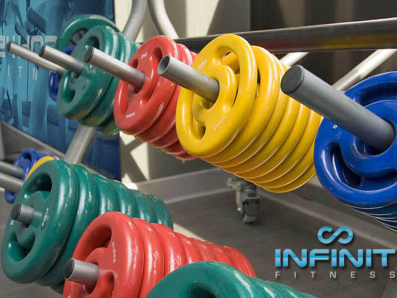 Barbell rack with colorful weights, INFINITI FITNESS logo visible.