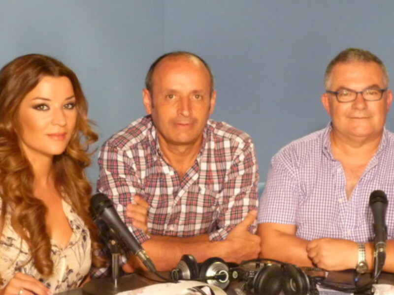Tres personas sentadas en una mesa con micrófonos, probablemente en un evento informativo o de prensa.