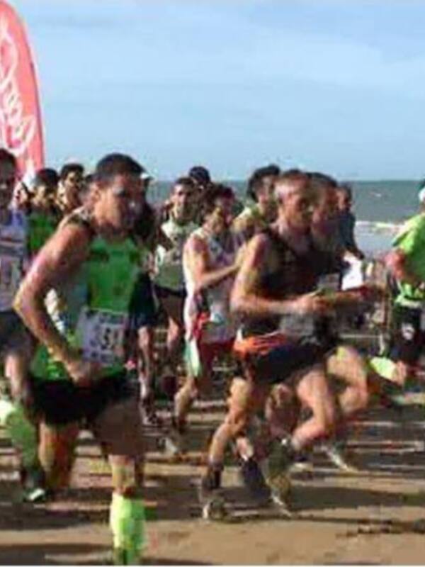 Corredores en una maratón costera, con banderas de la marca de relojes en el aire. El mar y las nubes forman un fondo hermoso para este evento deportivo.