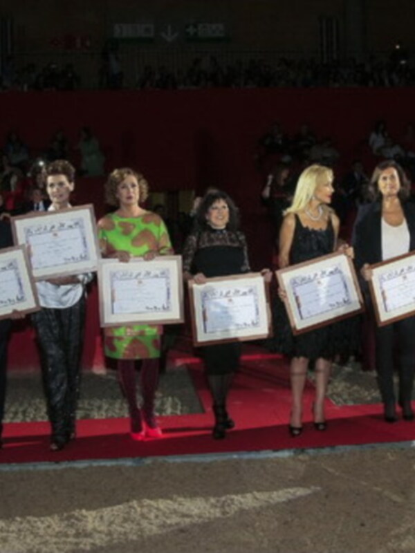 Premiación en ceremonia de gala con participantes sosteniendo certificados en un escenario con audiencia en el fondo.
