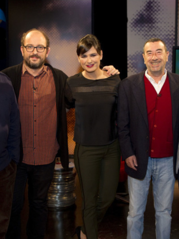 Personas en un estudio de televisión, posando frente a una pantalla con información.