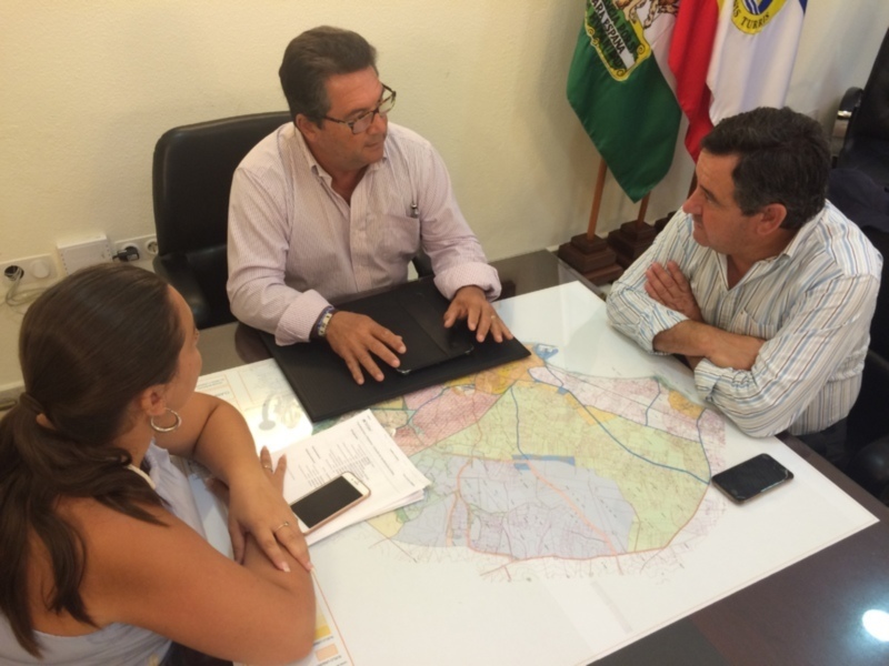 Dos personas discuten junto a un mapa de la región, con una bandera en el fondo.