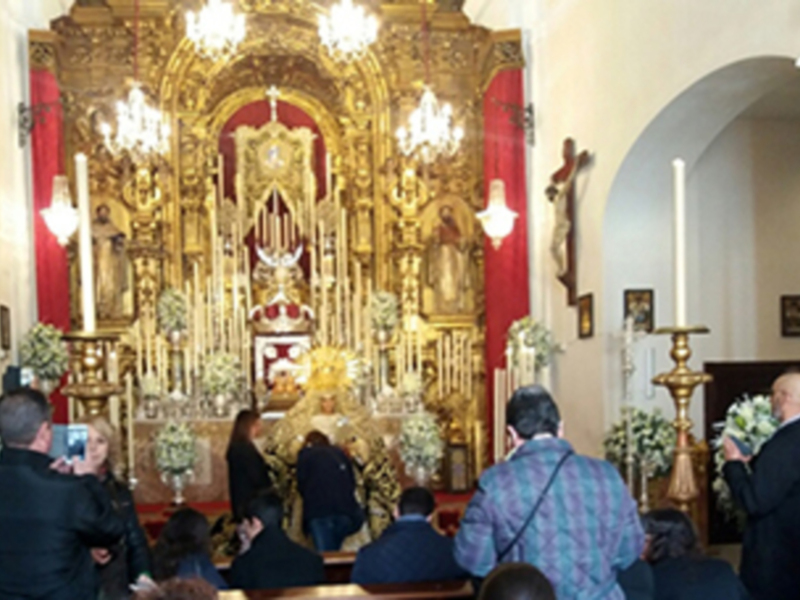 Una imagen de una iglesia con un altar dorado, flores y personas en el fondo.