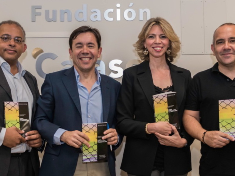 Tres personas sonrientes sosteniendo libros en una sala con una pared blanca y la palabra 'Fundación' en la pared.