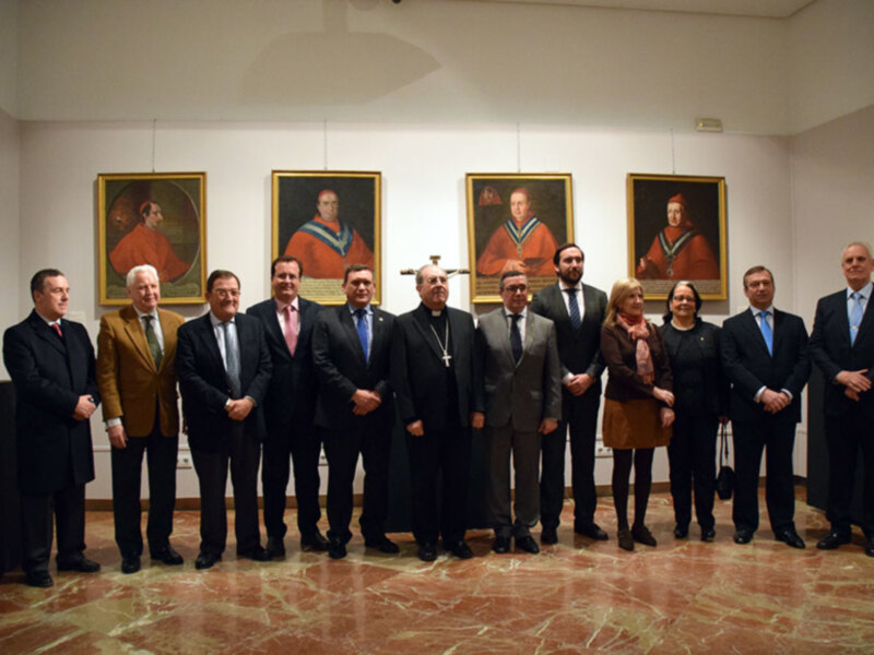 Una imagen de una reunión formal en un salón con suelos de mármol y paredes blancas. Se observa a una fila de personas, tanto hombres como mujeres, vestidos con trajes y chaquetas. En el fondo hay cuatro cuadros de retratos antiguos, lo que sugiere una atmósfera histórica o institucional. La iluminación es suave y el ambiente parece ser un lugar de reuniones oficiales o ceremonias.