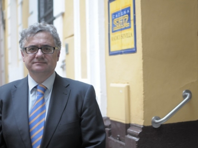 Un hombre en traje y corbata azul se encuentra frente a una puerta amarilla con un letrero de Sesta. La imagen sugiere un entorno profesional o empresarial.