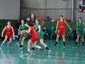 Jugadoras de baloncesto en acción durante un partido. El equipo rojo está defendiendo el balón mientras que el equipo verde ataca. La cancha es verde con líneas blancas de marcación.