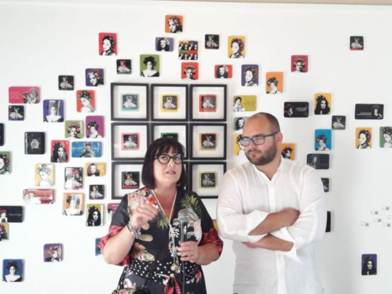 Dos personas frente a una pared decorada con fotos de diferentes artistas.