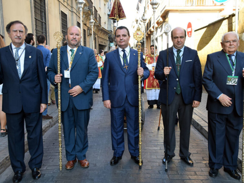 Oficiales con bastones de mando en una procesión religiosa en una calle urbana.