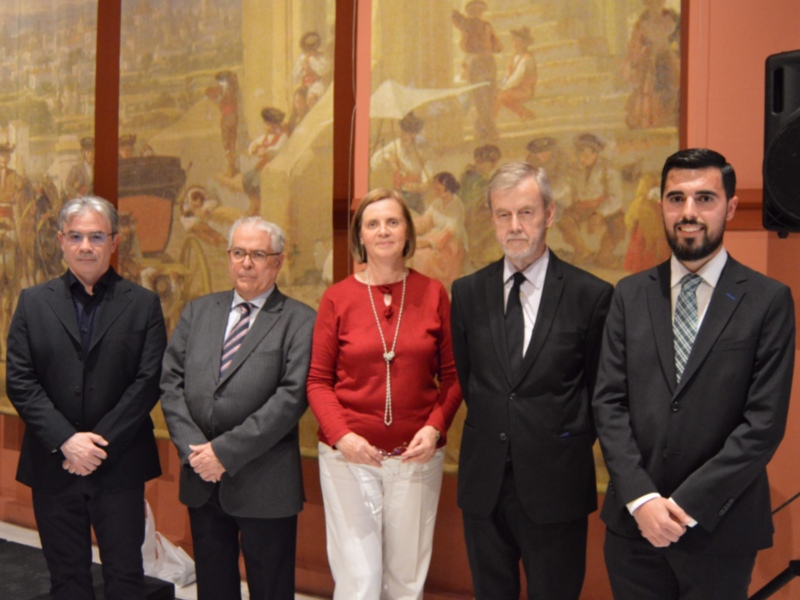 Una imagen de cuatro personas vestidas formalmente, posando frente a un mural histórico. La escena parece ser una reunión o evento oficial en un entorno decorado con elementos culturales.