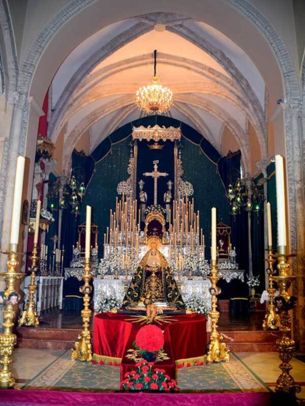 Interior de una iglesia con altar principal, candelabros dorados y flores rojas en el frente.