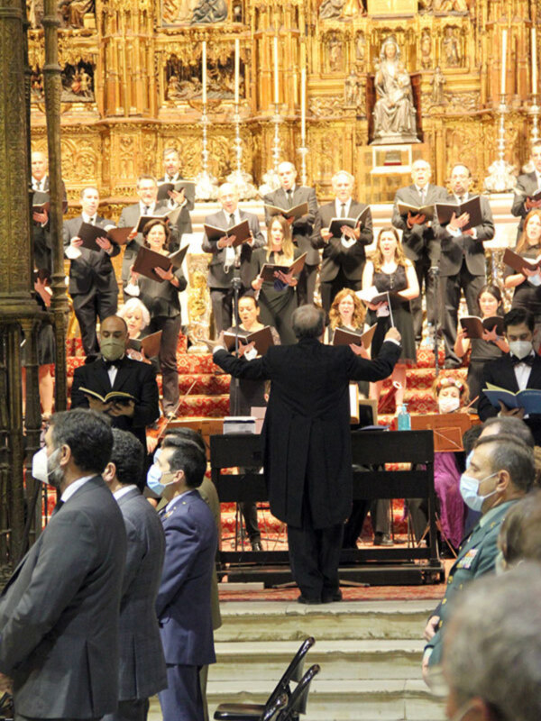 Imagen de un concierto en una iglesia con coros y músicos interpretando. La decoración es dorada y el público está atento a la actuación.