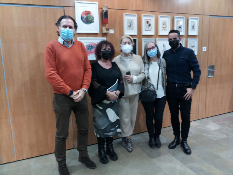 Una imagen de cuatro personas posando frente a un muro con cuadros. Todos están usando máscaras faciales y parecen estar en un lugar formal, posiblemente una oficina o sala de reuniones. La escena sugiere un evento formal o una reunión profesional en curso, posiblemente relacionado con el arte o la cultura.