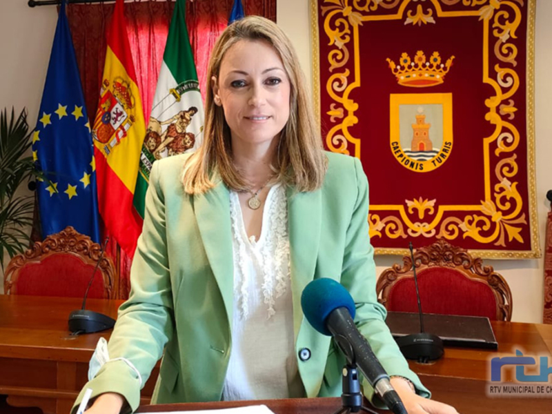 La alcaldesa de Chipiona, en una comparecencia ante los medios, con la bandera de Chipiona y la bandera de España al fondo.