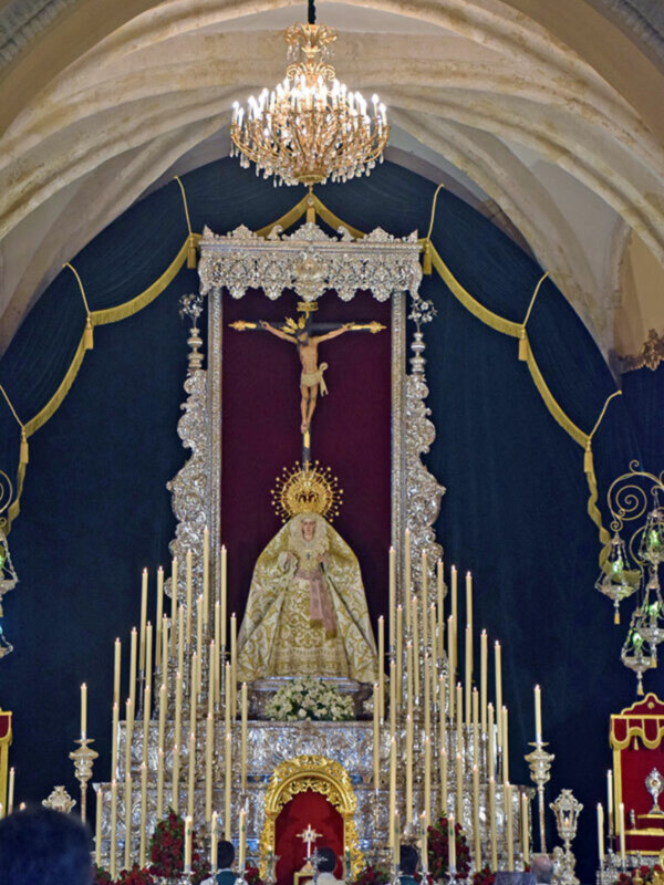Altar con imagen de la Virgen y crucifijo, velas encendidas, arco dorado y techo con detalles de cristal.