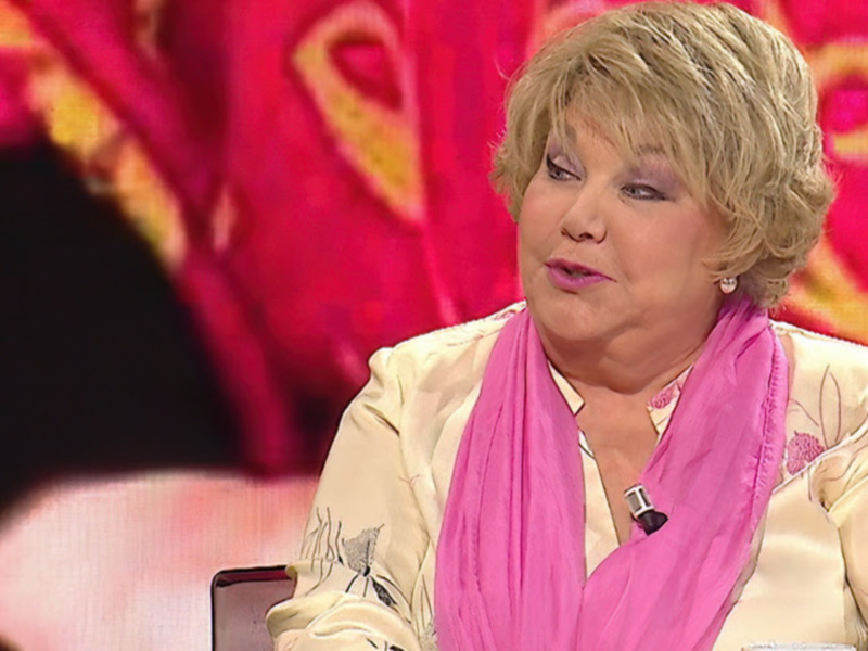 Persona hablando en un programa de televisión con fondo rojo y detalles florales.