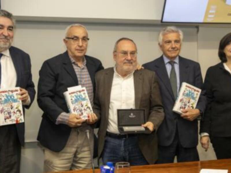 Presentación de un libro en una conferencia. Los presentadores sostienen el libro y sonríen, mientras otros asistentes observan la actividad. En el fondo, se ve una pantalla con texto que parece ser un título o subtítulo de la conferencia.