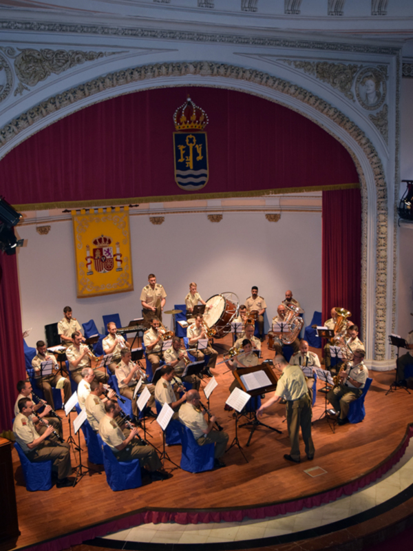 Orquesta militar en un escenario histórico con arcos y escudos.