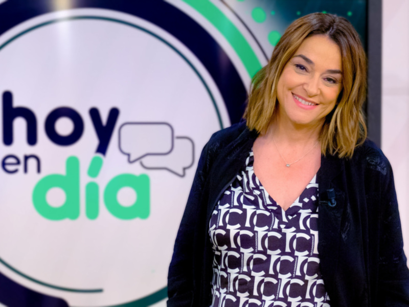 "La imagen muestra a una mujer sonriendo frente a un fondo con el texto 'hoy en día' y dibujos de mensajeros. La escena parece ser del programa 'Hoy en Día', una producción de Televisa."