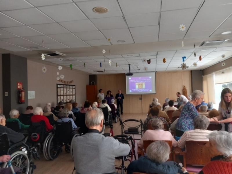 Conferencia en una sala de residentes con proyección en pantalla y audiencia atenta.