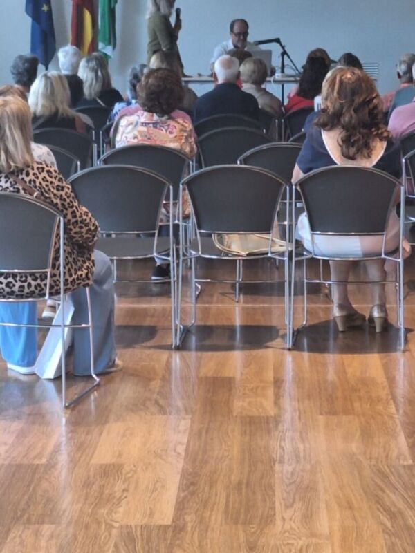 Una sala de conferencias con una pantalla proyectando imágenes, varias personas sentadas en sillas, banderas de diferentes países a la izquierda.