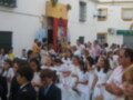 Una procesión religiosa en un pueblo, con jóvenes vestidos formalmente y una iglesia al fondo.