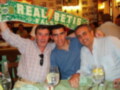 Tres personas celebran con una bufanda del Real Betis en un ambiente acogedor de restaurante.