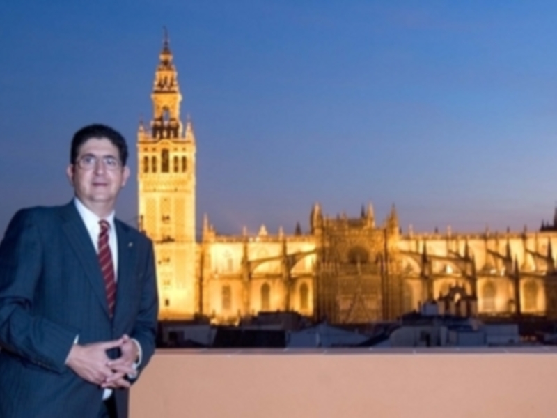 Un hombre en traje posa frente a la Giralda de Sevilla, iluminada por el atardecer.