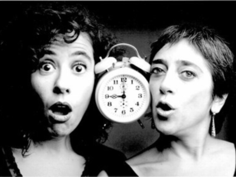 Dos personas sorprendidas sostienen un reloj de alarma, capturando el momento del despertar.